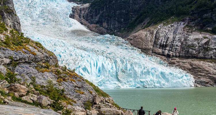 Personas caminando cerca de un gran glaciar y lago.
