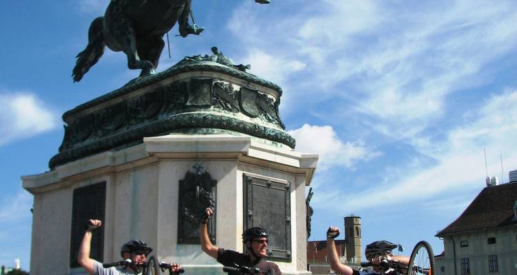Ciclistas posando delante de una estatua con las manos levantadas