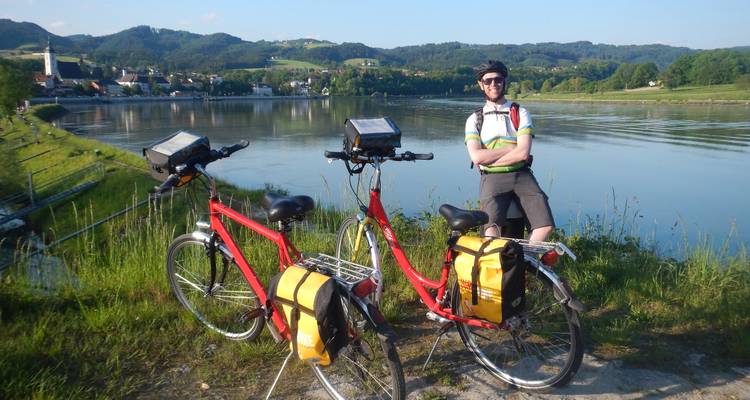 Ciclista posando con bicicletas junto a un río con colinas al fondo