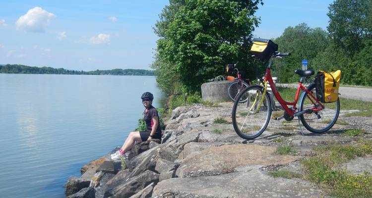 Persona sentada en unas rocas junto a un lago con una bicicleta aparcada al lado