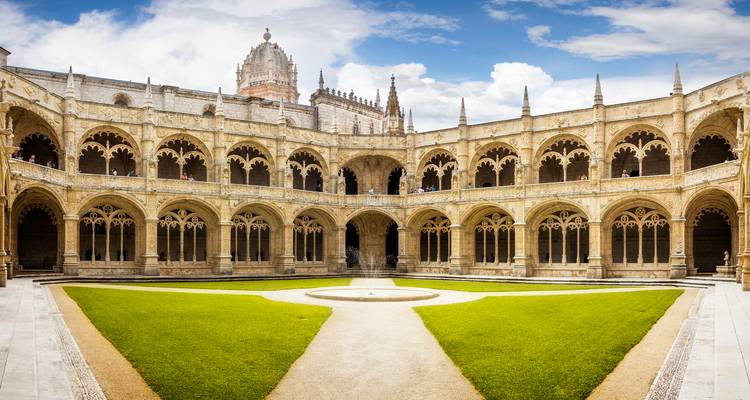 Vue panoramique d'un cloître historique avec une fontaine et une pelouse.