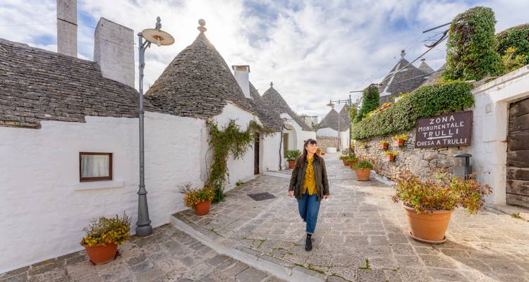 Person, die in Alberobello zwischen Trulli-Häusern spaziert.