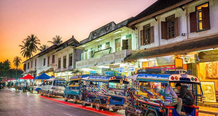 Des tuk-tuks colorés garés dans un marché de rue animé au coucher du soleil.