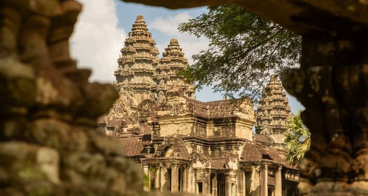 Une vue d'Angkor Vat à travers des ruines anciennes et des arbres.