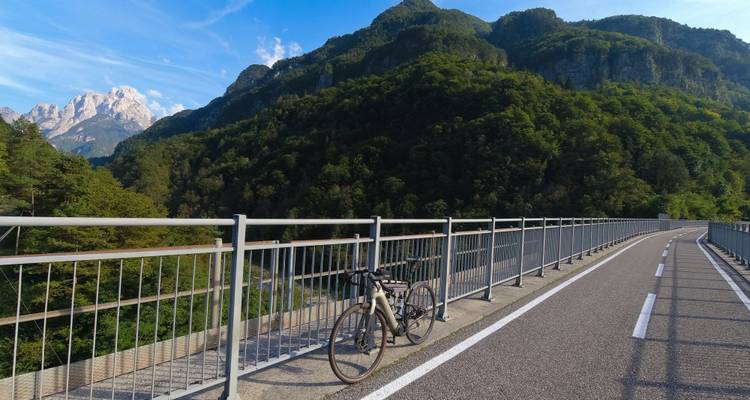 Brug over een vallei met een geparkeerde fiets en bergachtige achtergrond.