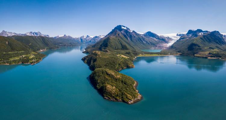 Panorama aérien d'un fjord turquoise flanqué de péninsules boisées et de pics couronnés de glaciers en Norvège.