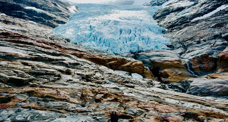 Vue rapprochée d'une face de glacier bleu s'écoulant en cascade sur des couches de roches multicolores.