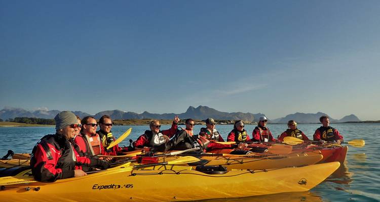 Groupe de kayakistes en kayaks de mer jaunes souriant sur une eau bleue calme sous un ciel dégagé.