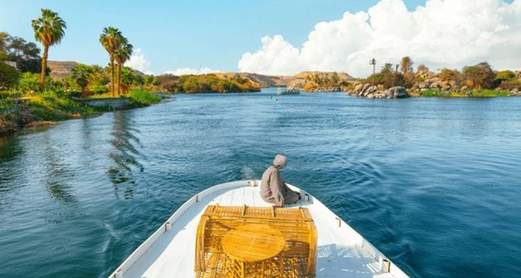Personne se détendant à l'avant d'un bateau sur une rivière avec des palmiers.