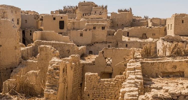 Ancien village désertique partiellement en ruine avec des structures en briques de terre crue.