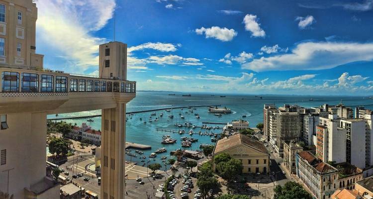 Panorámica urbana que presenta la icónica torre del ascensor con vista a un puerto deportivo lleno de barcos y la bahía azul profundo más allá.