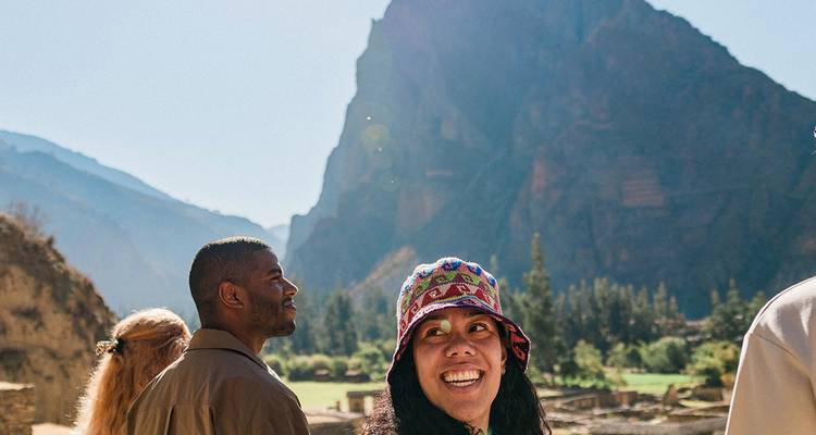 Los viajeros admiran las terrazas de piedra iluminadas por el sol bajo los imponentes acantilados de Ollantaytambo en el Valle Sagrado de Perú.
