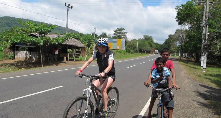 Persona pedaleando junto a niños en una carretera rural.