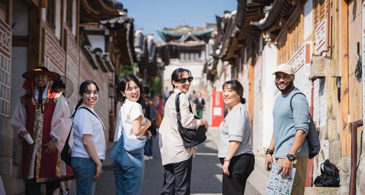 Pequeño grupo de viajeros sonrientes caminando por un callejón tradicional coreano hanok con techos de madera ornamentados