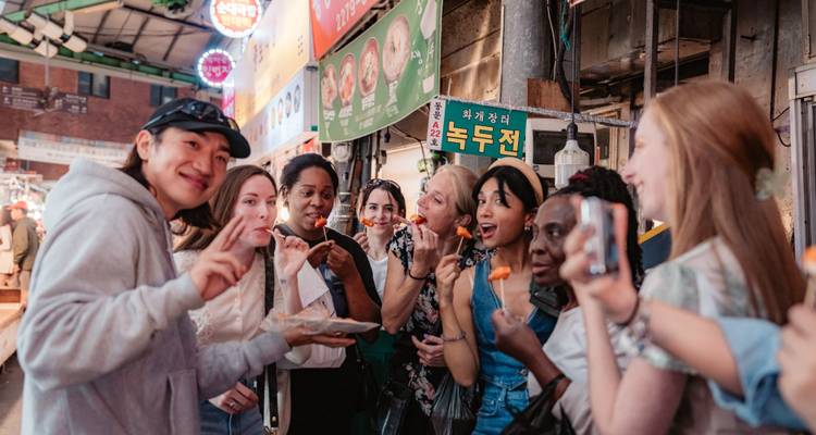 Grupo de turistas probando comida callejera en un bullicioso mercado coreano, posando de manera divertida para la cámara