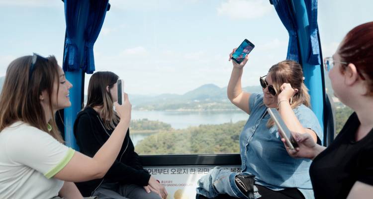 Amigos dentro de una góndola de teleférico tomando fotos de un paisaje de lago y bosque abajo