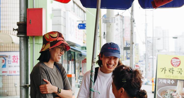 Viajeros conversando y riendo con un vendedor local bajo una sombrilla colorida en una calle coreana