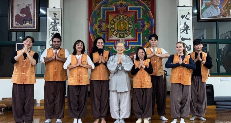 Visitantes vestidos con uniformes de estancia en el templo posan con un monje budista sonriente en un salón colorido