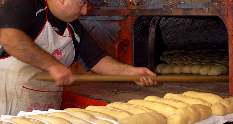 Panadero metiendo hogazas de pan en un horno tradicional.