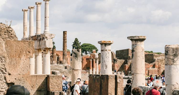 Turistas explorando ruinas con columnas al fondo.