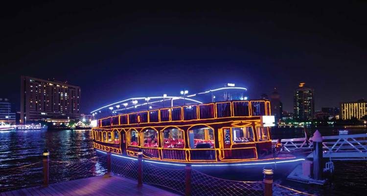 Barco iluminado en el agua por la noche con el horizonte de la ciudad.
