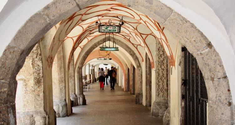 Arco de piedra con techo decorativo y personas caminando a través.