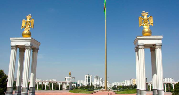 Deux piliers surmontés d'aigles encadrant un drapeau national avec des bâtiments urbains en arrière-plan.