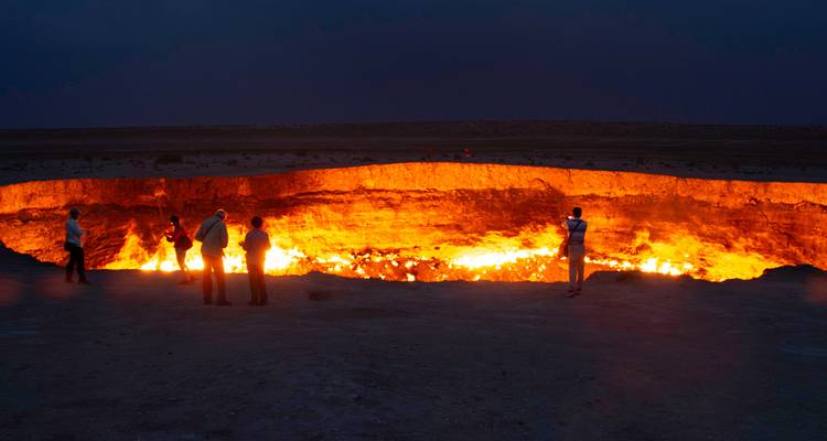 Un groupe de personnes observant le cratère gazier enflammé de Darvaza la nuit.