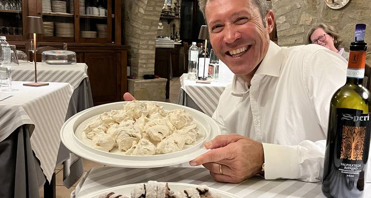 Un hombre sonriendo mientras sostiene un plato grande de comida en un ambiente de restaurante.