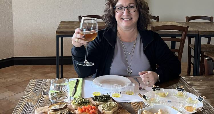 Mujer disfrutando de una variedad de comidas con una copa de bebida en una mesa de comedor.