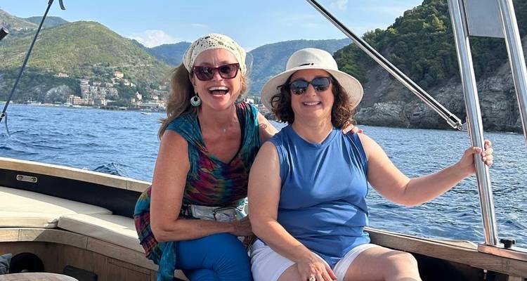 Dos mujeres disfrutando un paseo en bote con paisaje costero de fondo.