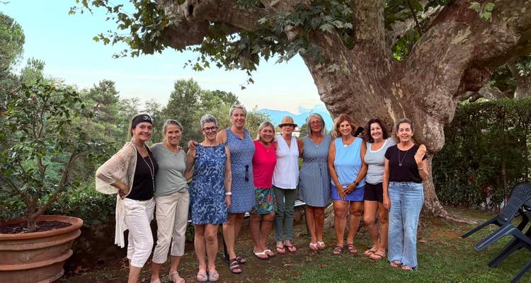 Grupo de mujeres de pie bajo un gran árbol en un jardín.