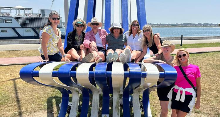 Grupo de mujeres posando en una gran escultura azul y blanca junto al río.