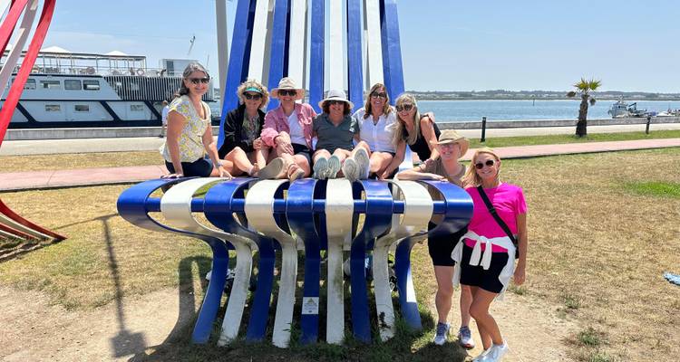 Grupo de mujeres posando en una gran escultura azul y blanca junto al río.