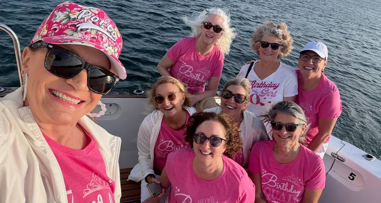 Grupo de mujeres con atuendos rosa a juego en un barco.