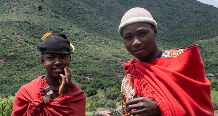 Twee personen in traditionele kledij met een weelderige groene heuvel op de achtergrond.