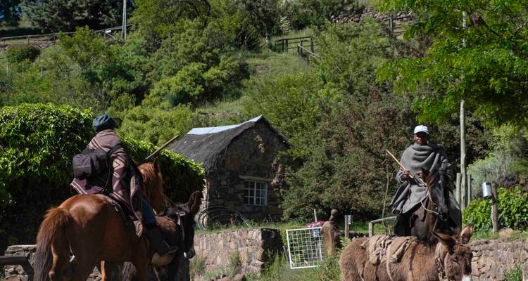 Twee personen te paard die door een landelijk bergachtig gebied rijden.