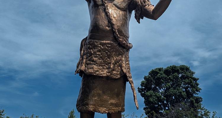 Een standbeeld van een persoon met een opgeheven arm tegen een blauwe lucht.