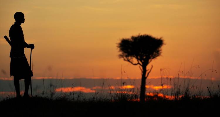 Silhouette einer Massai-Person mit einem Speer bei Sonnenaufgang.