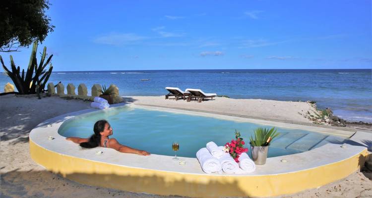 Person entspannt sich in einem Pool am Strand unter sonnigem Himmel.