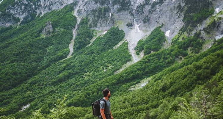 Hombre caminando por senderos de montaña boscosos y densos de color verde