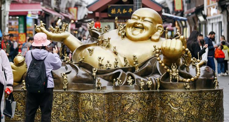 Groot gouden lachende Boeddhabeeld omringd door bezoekers die foto's maken.