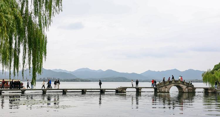 Vue panoramique d'un pont enjambant un lac avec des personnes qui le traversent, sur fond de montagnes.