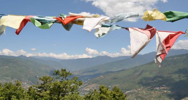 Drapeaux de prière colorés sur un fond de montagnes luxuriantes et de ciel dégagé.