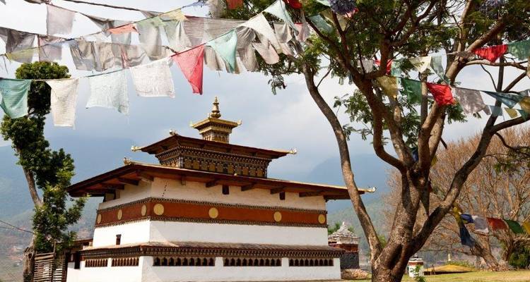 Bâtiment bhoutanais traditionnel avec drapeaux de prière, entouré d'arbres.