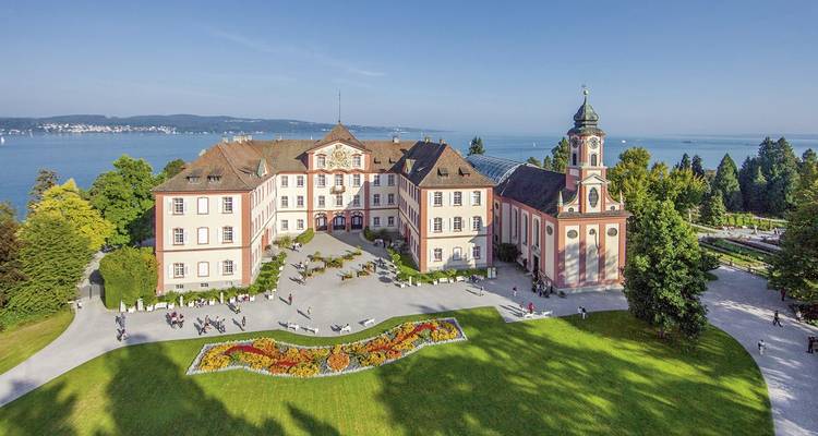 Barockschloss und Kirche auf der Insel Mainau, umgeben von gepflegten Rasenflächen und Blumenbeeten am See.