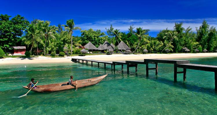 Dos personas en una canoa sobre un mar turquesa cristalino dirigiéndose hacia una playa tropical.