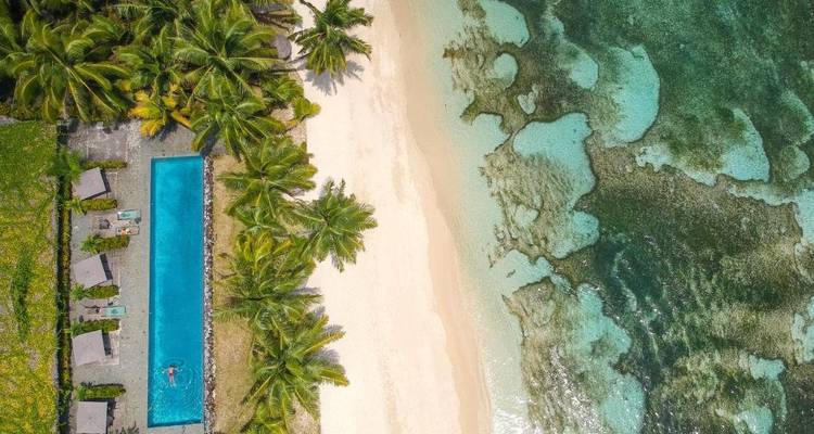 Vista aérea de una playa tropical con una piscina y olas del océano.