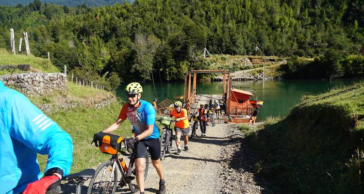 Groupe de cyclistes poussant leurs vélos sur un sentier au bord d'une rivière.