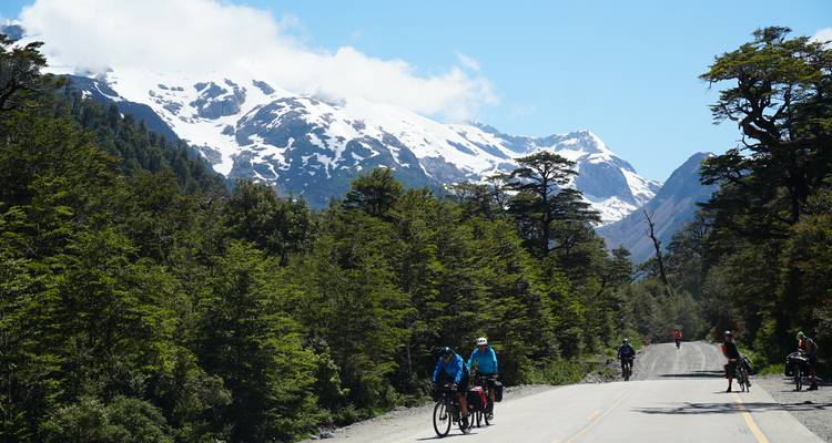 Groupe de cyclistes sur une route entourée de montagnes boisées.